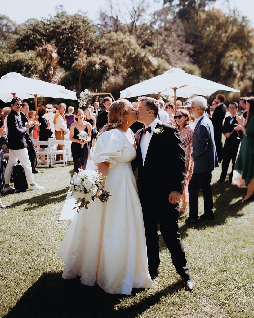 Couple kissing on the lawn after the ceremony as guests applaud