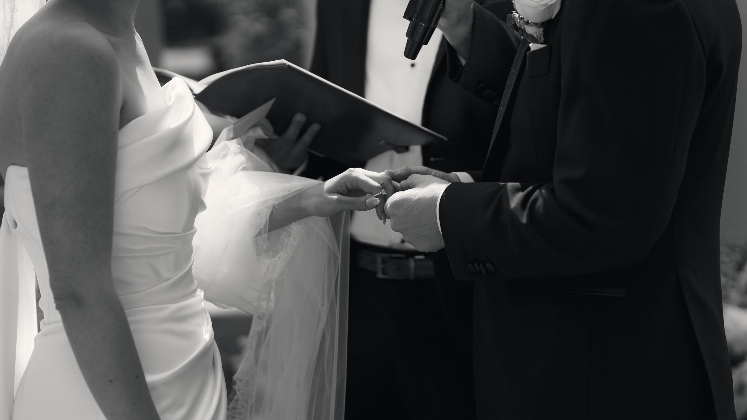 Close detail of a ring being placed on the bride’s hand during the ceremony, black and white