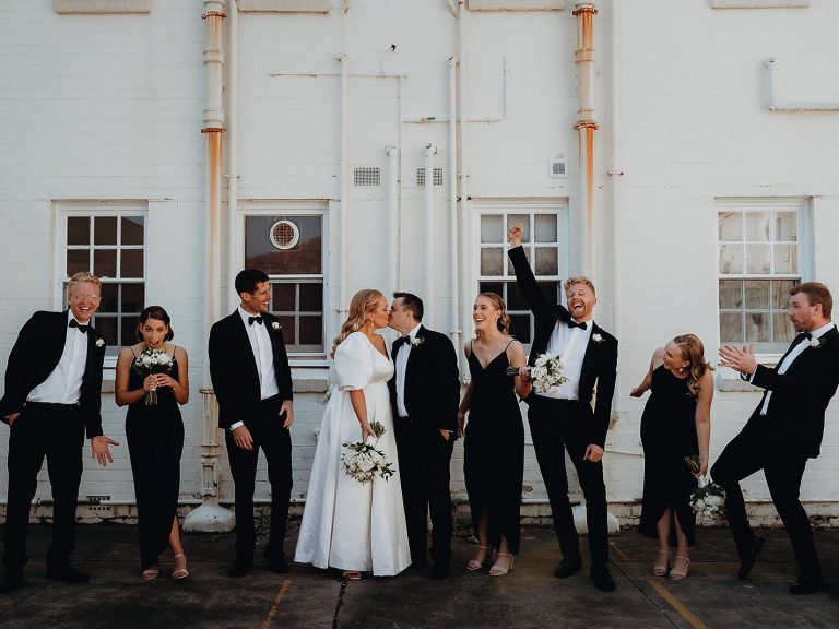 Bridal party laughing together against a white brick wall