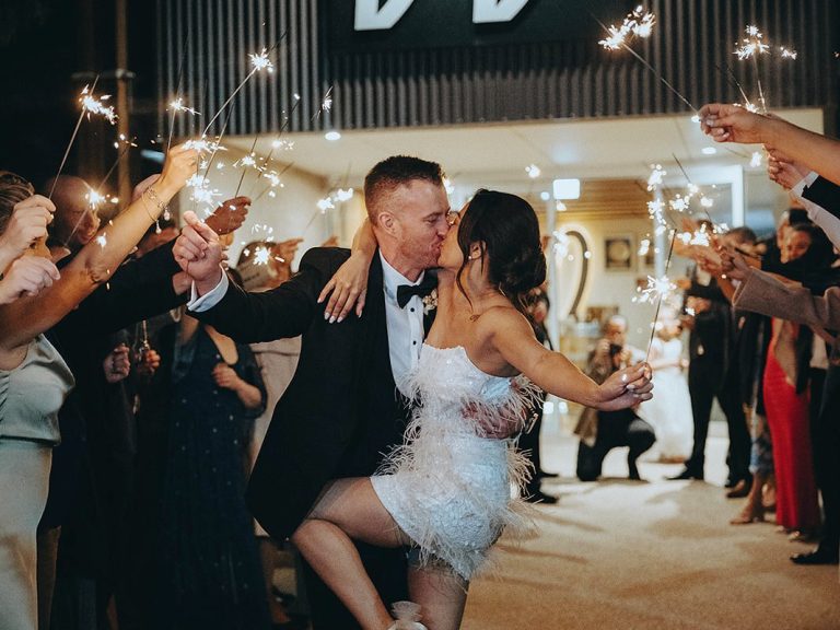 Newlyweds kissing under an arch of sparklers held by guests